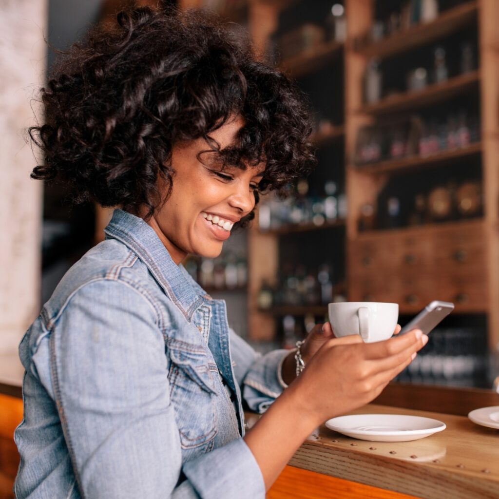 Photograph of a woman sipping coffee while reading something on her phone. Image is intended to emphasize the power of a mobile-friendly website. 