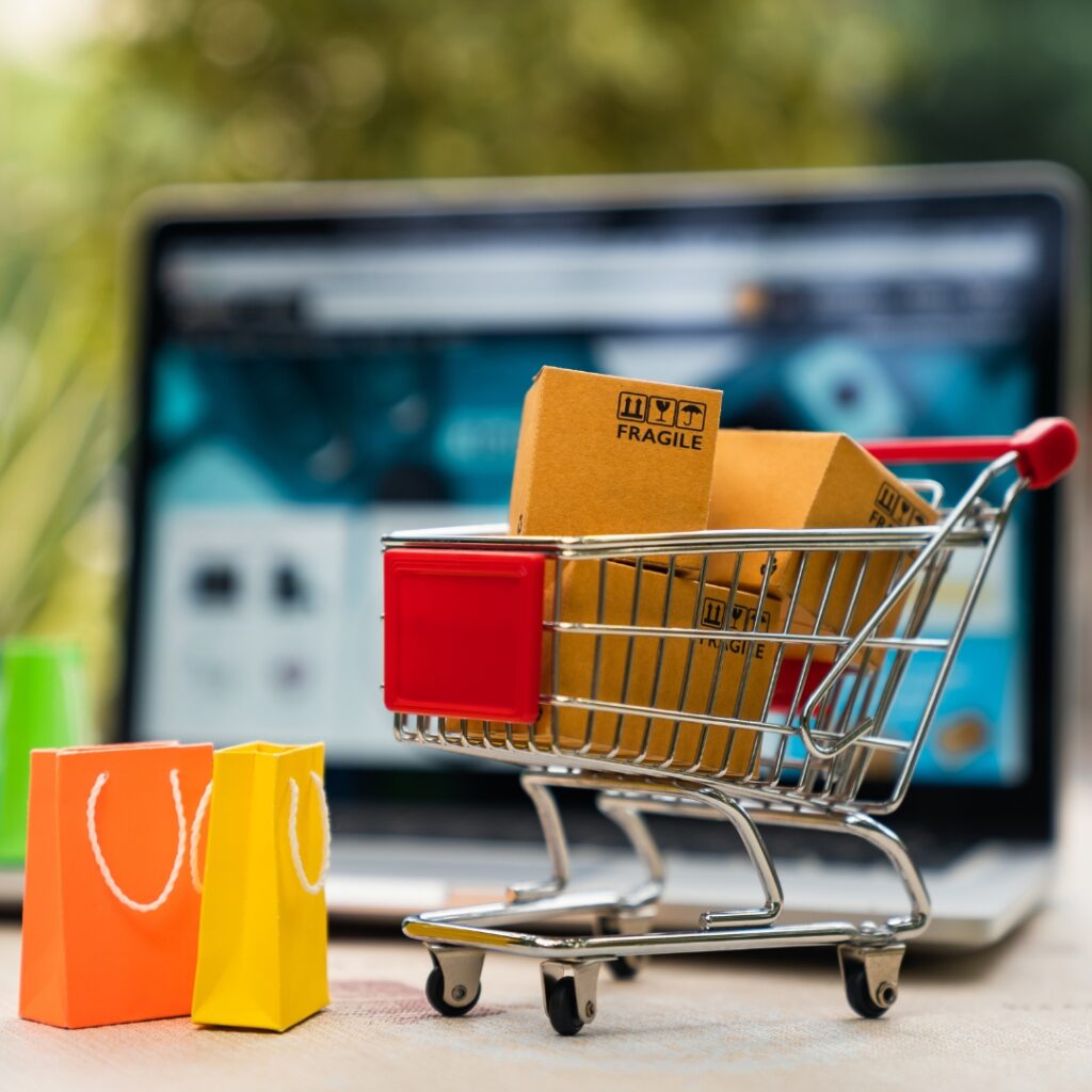 A photo of small shopping cart with packages in front of a laptop. Image illustrates the power of online conversions - like making a sale. 